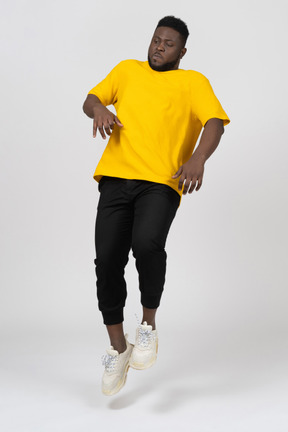 Vista frontal de un joven de piel oscura con camiseta amarilla saltando hacia atrás