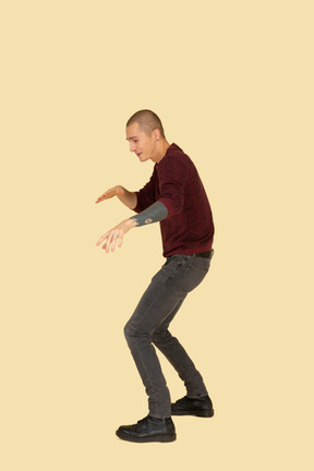 Side view of a cautious young man dressed in red pullover outstretching his hands