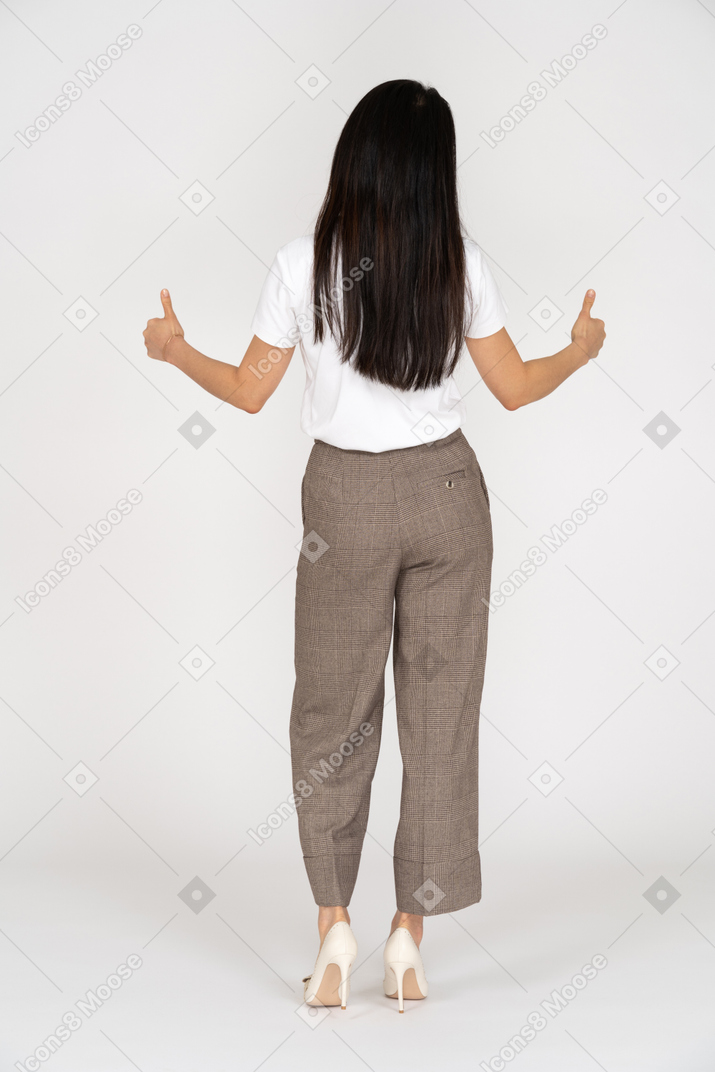 Vista posteriore di una giovane donna sorridente in calzoni e t-shirt che mostra i pollici in su