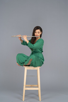 Comprimento total de uma jovem tocando clarinete sentada com as pernas cruzadas em uma cadeira de madeira