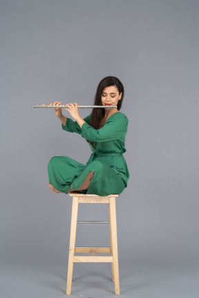 Full-length of a young lady playing the clarinet sitting with her legs crossed on a wooden chair