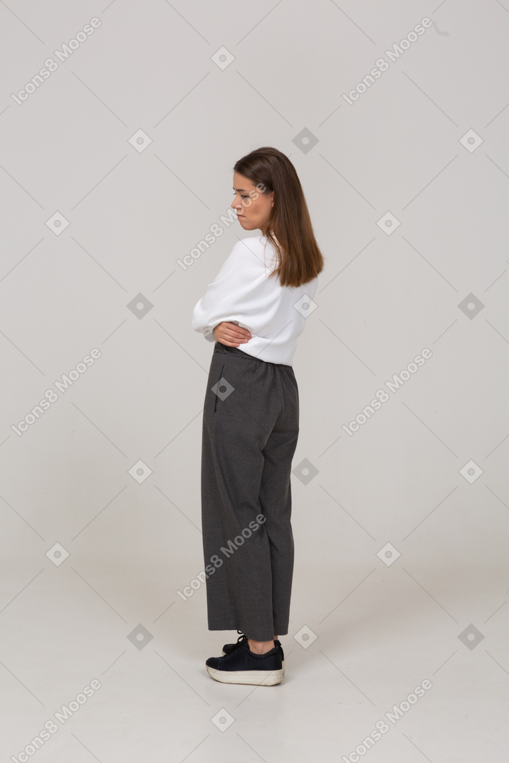 Vista posterior de tres cuartos de una señorita molesta en ropa de oficina poniendo las manos sobre el vientre