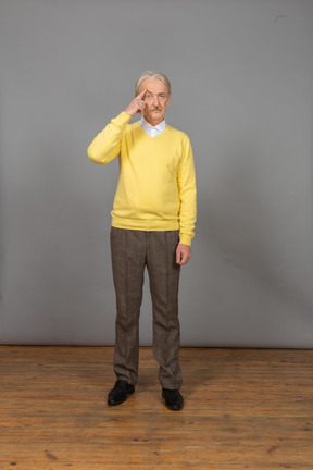 Front view of an old thoughtful man wearing yellow pullover and touching forehead