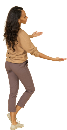 Three-quarter back view of a dark-skinned young female outstretching her hands