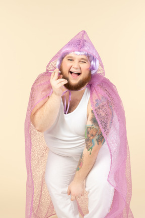 Laughing young overweight man in fairy cape holding a cigarette