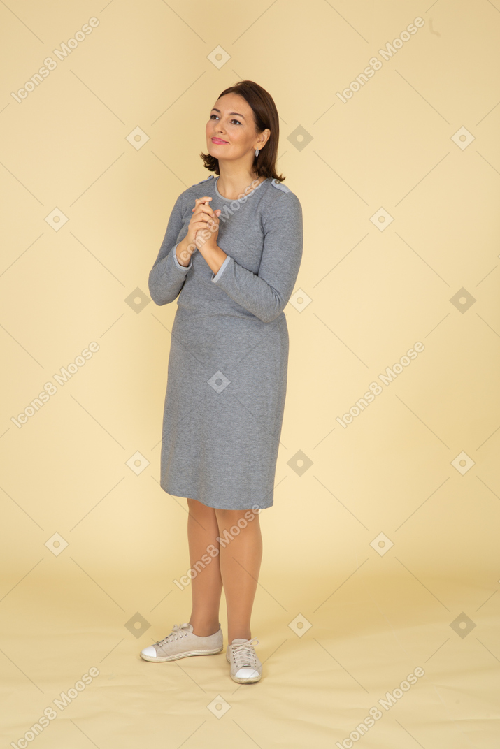 Vista lateral de uma mulher de vestido cinza fazendo gesto de oração
