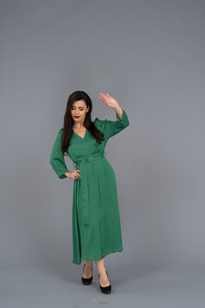 Vista frontal de uma jovem de vestido verde colocando a mão no quadril enquanto levanta a mão