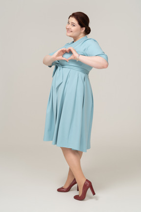 Vista lateral de uma mulher de vestido azul mostrando um gesto de coração