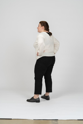 Rear view of a plump woman in casual clothes standing with hands on hips