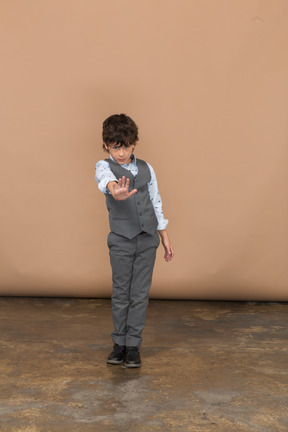 Vista frontal de um menino de terno cinza mostrando o gesto de parada