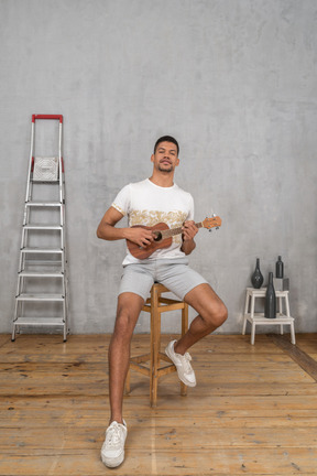 Vorderansicht eines mannes, der auf einem hocker sitzt und ukulele spielt