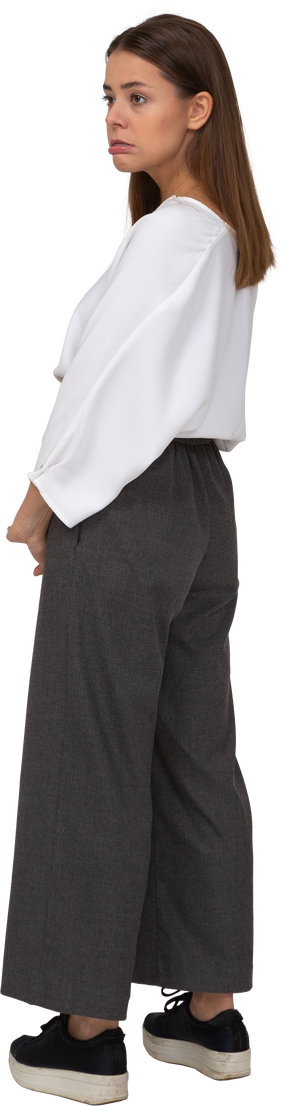 Vista posteriore di tre quarti di una giovane donna in abiti da ufficio in piedi con le labbra abbassate