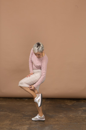 一个穿着休闲服的女人站在一条腿上摸她的鞋子的侧视图