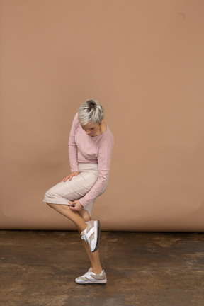 Side view of a woman in casual clothes standing on one leg and touching her shoe