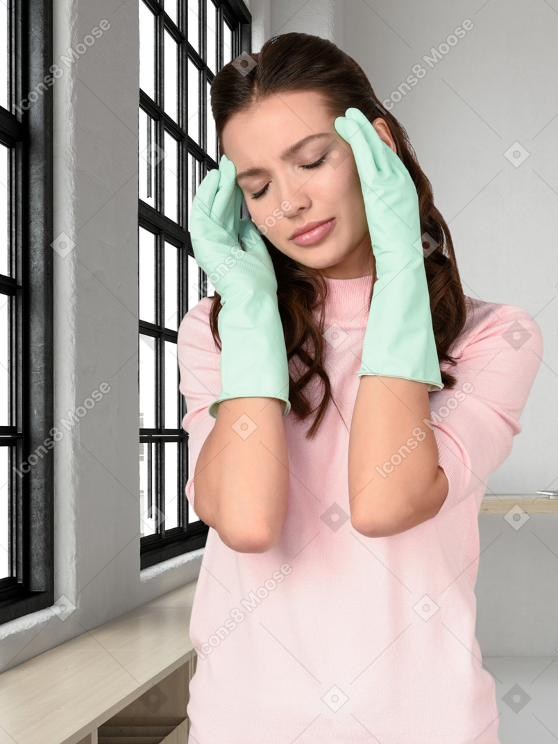 A distressed woman in a pink shirt and green gloves holding her head