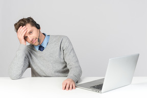 Call center operator sitting at office desk and leaning head on hand