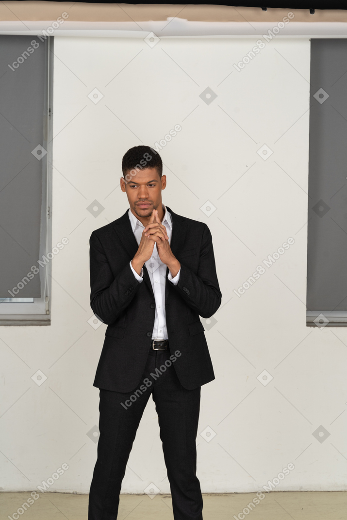 Pensive young man in black suit standing with his hands folded