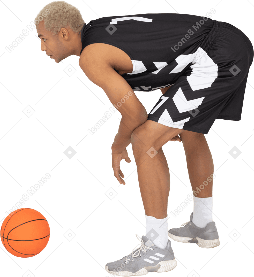 Side view of a young male basketball player standing by the ball