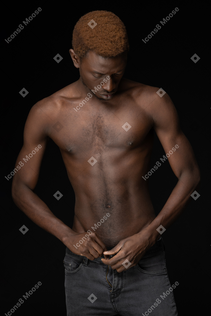 Close-up de um homem africano fechando o zíper das calças e olhando para o lado