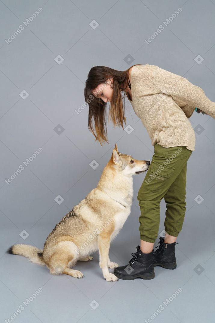 De cuerpo entero de una hembra joven inclinada sobre su perro y mirando hacia abajo
