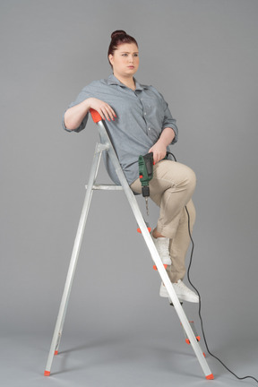Young woman sitting on stepladder with a screw driver