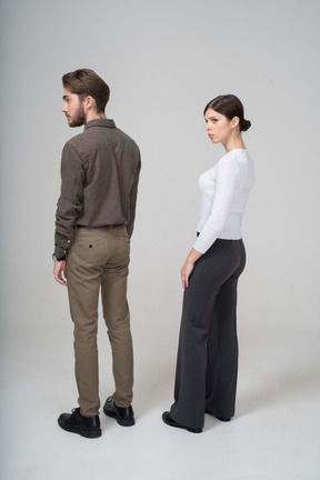 Three-quarter back view of a worried young couple in office clothing standing still