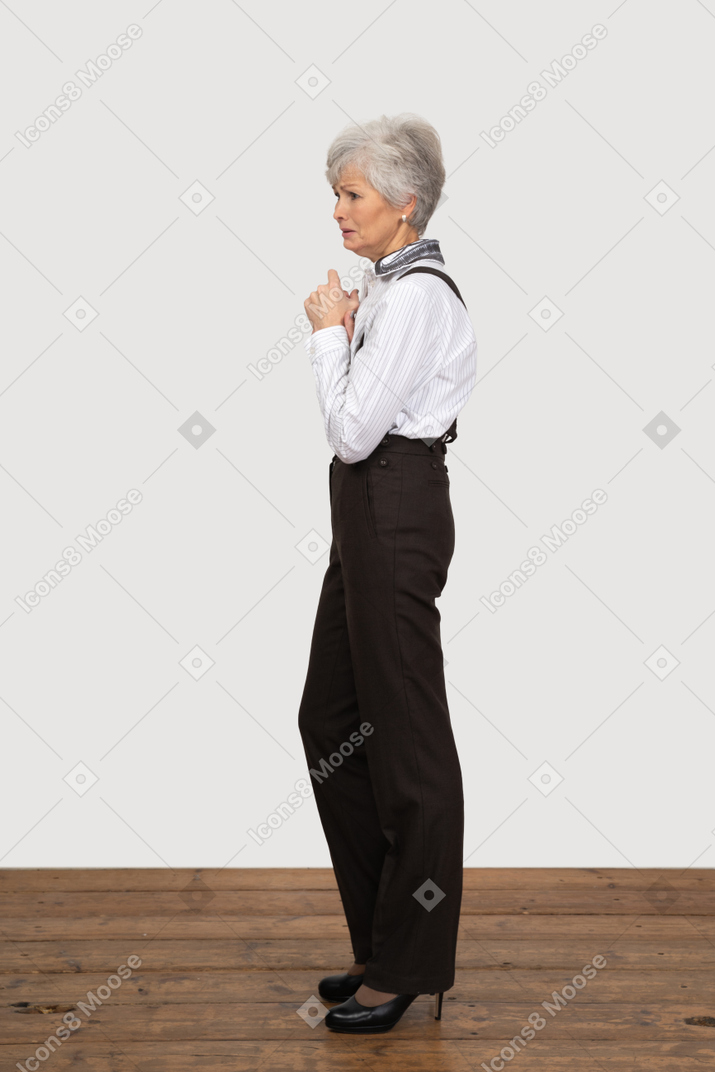 Seitenansicht einer besorgten alten dame in der bürokleidung, die hände zusammenhält