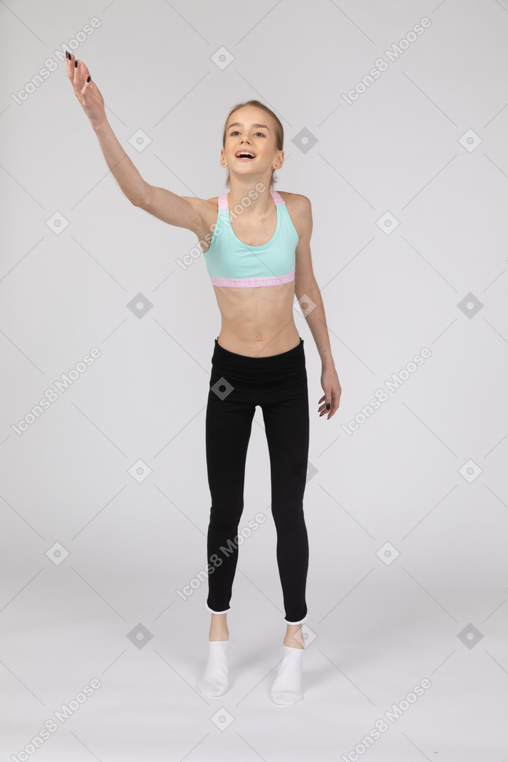 Вид сбоку девушки-подростка в спортивной одежде, сидящей на корточках и кладущей руки на бедра