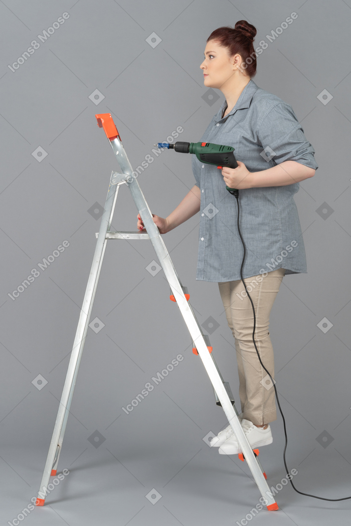 Woman standing sideways on stepladder and holding screw driver