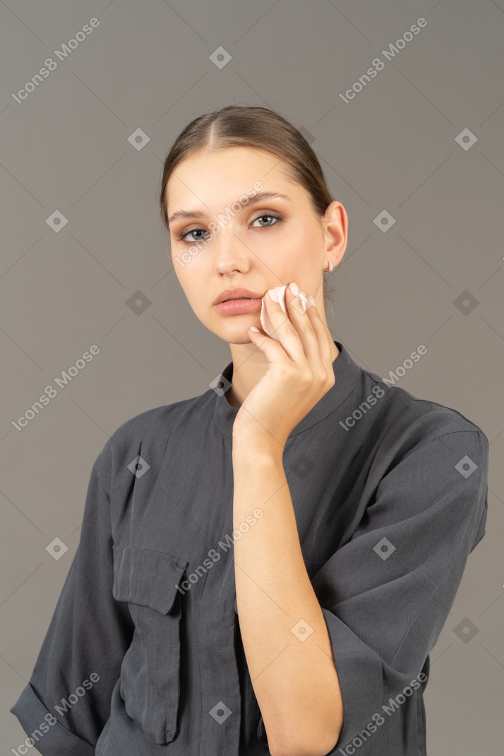 Vista de três quartos de uma jovem em um macacão removendo a maquiagem