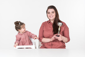 Madre y su pequeña hija sentada a la mesa con una copa de premio