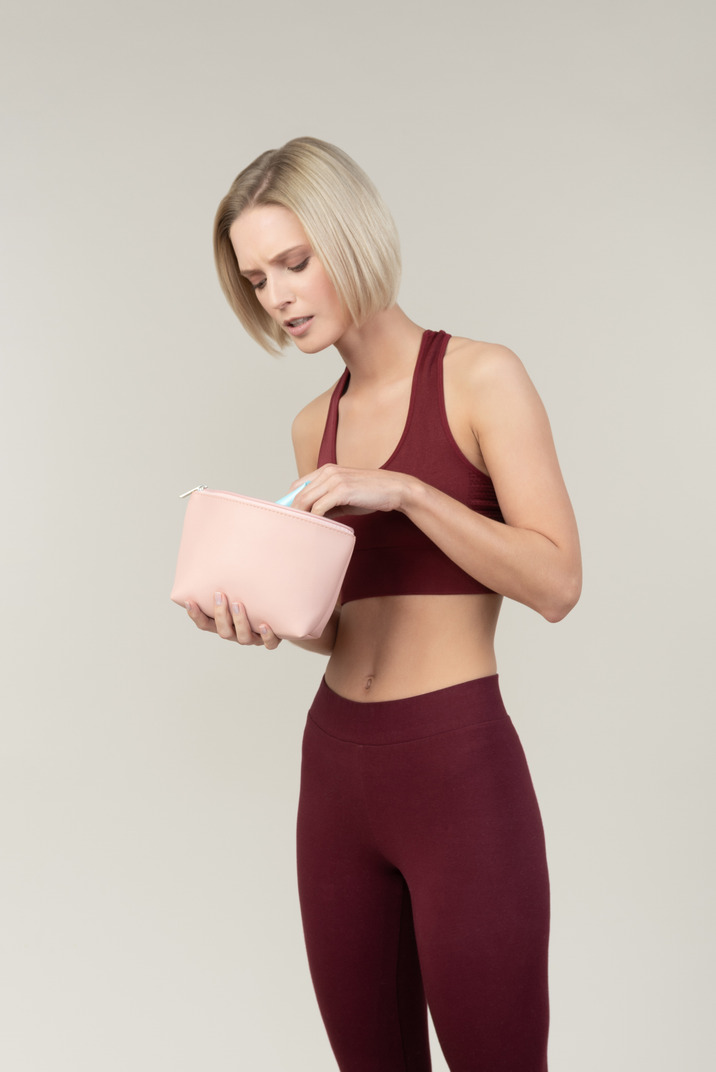 Pensive young woman in sportswear holding cosmetic bag