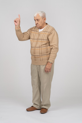 Front view of an old man in casual clothes pointing up with finger