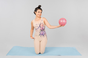 Молодая индийская гимнастка сидит на коврике для йоги и держит мяч