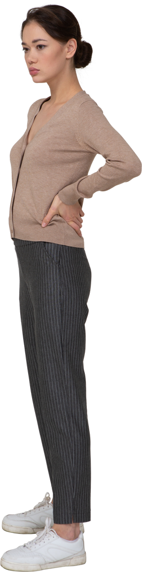 Vista di tre quarti di una giovane donna in pullover e pantaloni che mette le mani sui fianchi