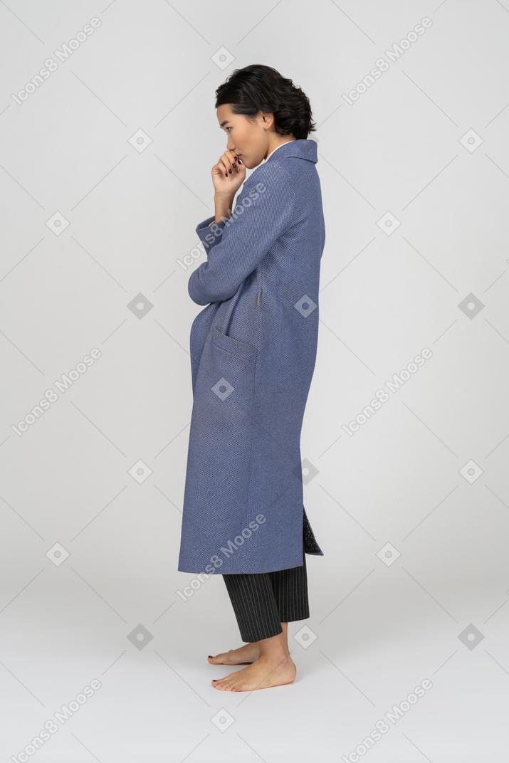Side view of a woman in coat with hand next to mouth