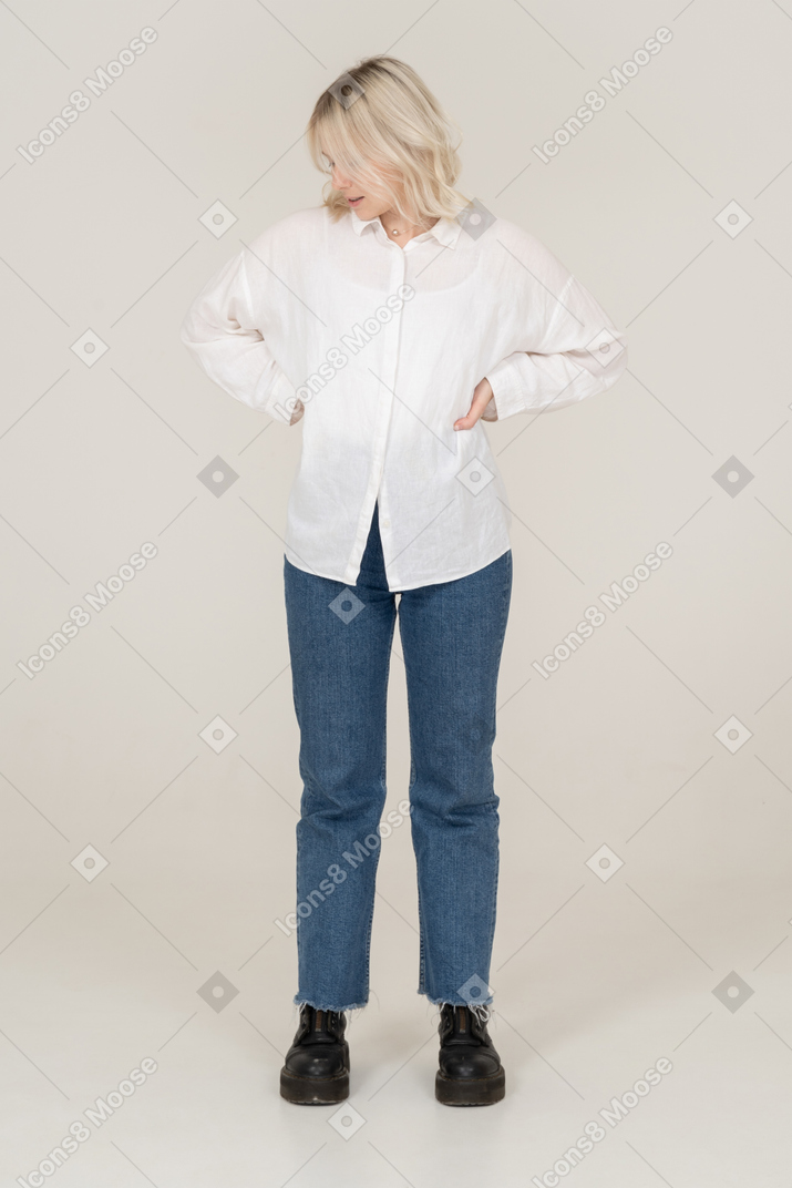 Front view of a blonde female in casual clothes putting hands on hips and looking down to the left