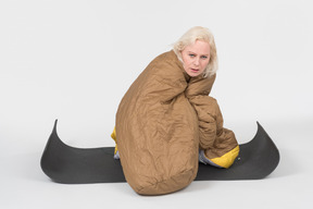 Mature woman sitting on tourist mat wrapped in blanket