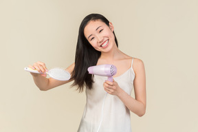 Young asian woman drying and styling hair with hair dryer