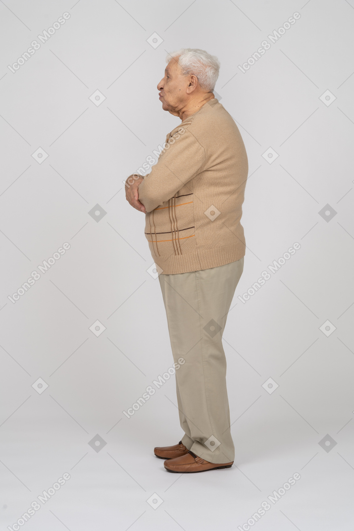 Side view of an old man in casual clothes blowing a kiss