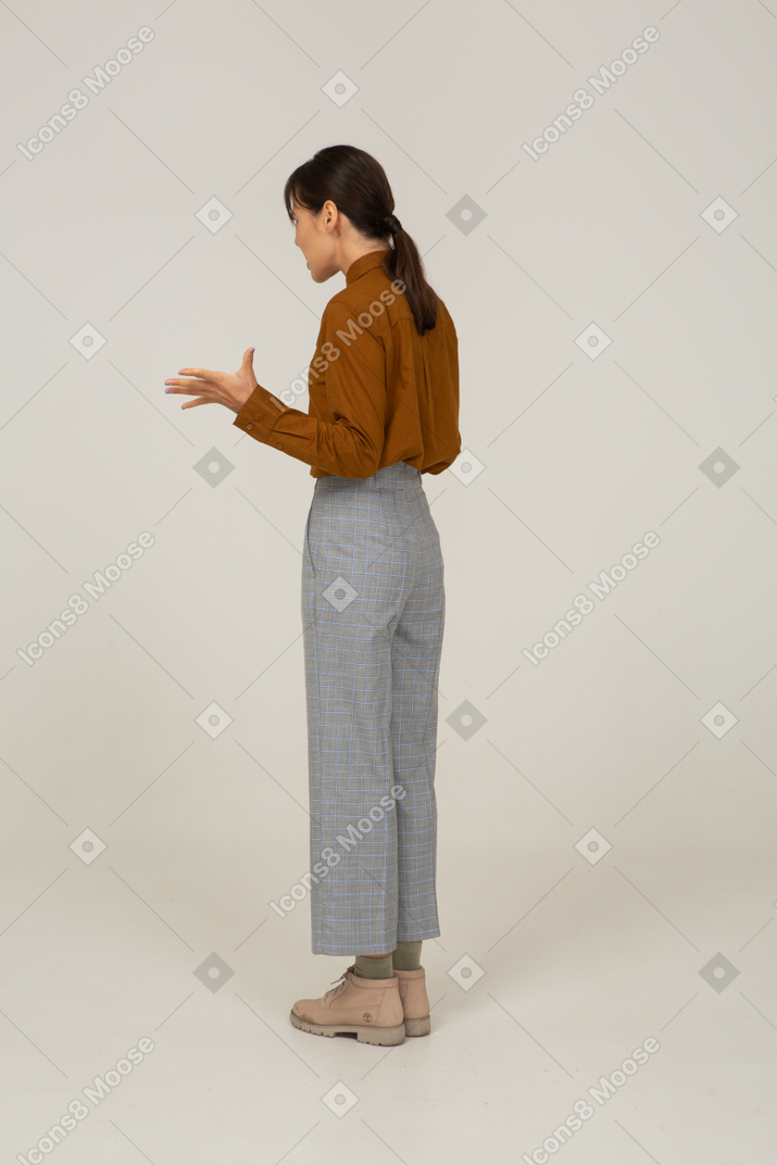 Three-quarter back view of a young gesticulating asian female in breeches and blouse