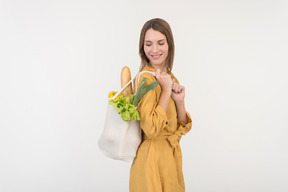 Jovem mulher segurando sacola de compras com legumes e olhando para baixo