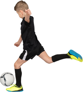 Vista lateral de um garoto com uniforme de futebol chutando uma bola