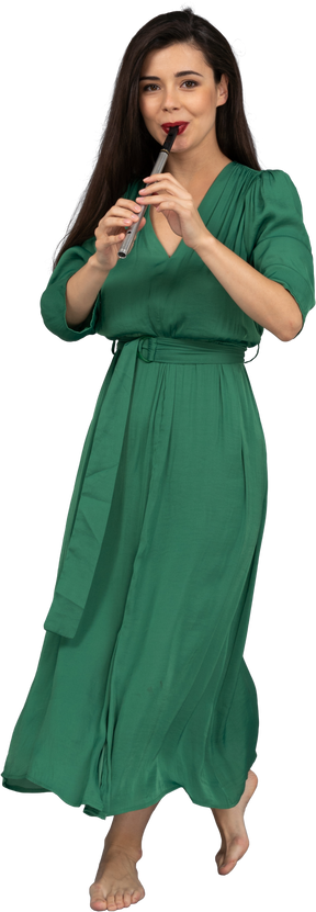 Vista frontale di una giovane donna che cammina in abito verde che suona il flauto