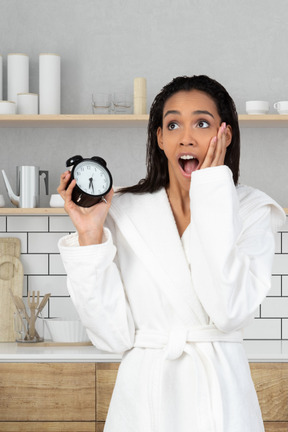 A woman in a bathrobe holding an alarm clock