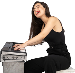 Vista lateral de una joven sentada sonriente en traje negro mientras toca el piano