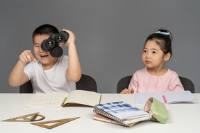 Garçon qui rit en regardant à travers des jumelles à côté d'une petite fille