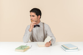 Pensive adult student sitting at the table with opened book