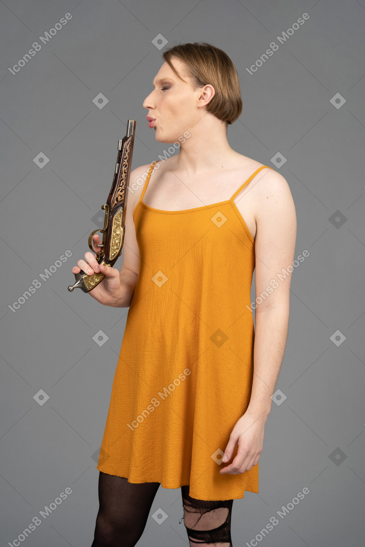 Non-binary person in orange dress blowing out gun smoke