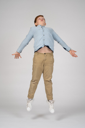 A boy in casual clothes jumping with his arms outstretched